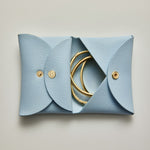 Blue leather jewelry pouch with gold rings on a light gray background