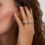 A close-up lifestyle shot of a woman's hand and ear wearing a delicate gold ring adorned with small blue gemstones.