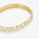 A close-up of a gold bangle bracelet featuring a row of bezel-set marquise and round clear stones, photographed on a clean white background.