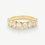 A yellow gold eternity ring featuring seven round-cut diamonds set in a continuous row on a polished band, shown against a clean off-white background.