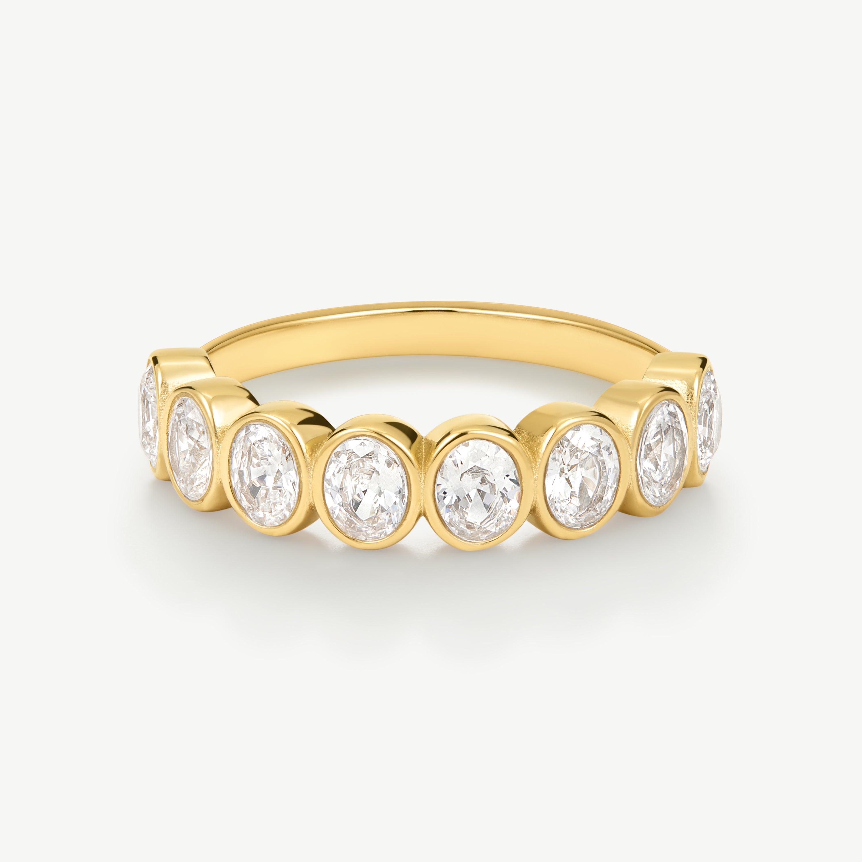 A yellow gold eternity ring featuring seven round-cut diamonds set in a continuous row on a polished band, shown against a clean off-white background.