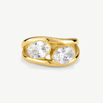 A yellow gold ring featuring two large, round-cut clear gemstones in a split setting, shown on a light gray background.