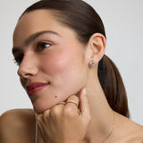Woman wearing diamond earrings and a ring, with a neutral background